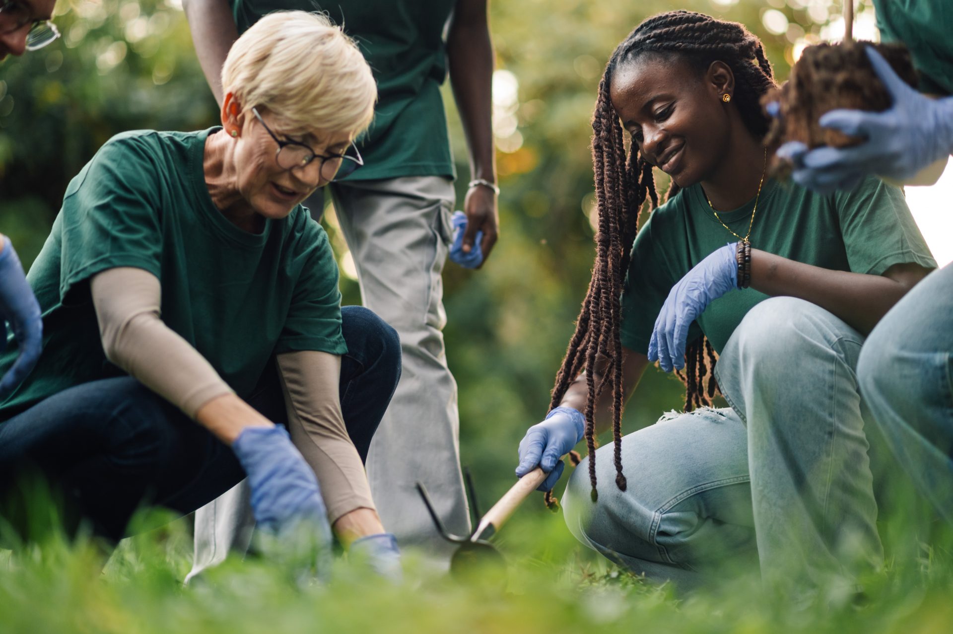 Two volunteers planting a seedling together in tall grass